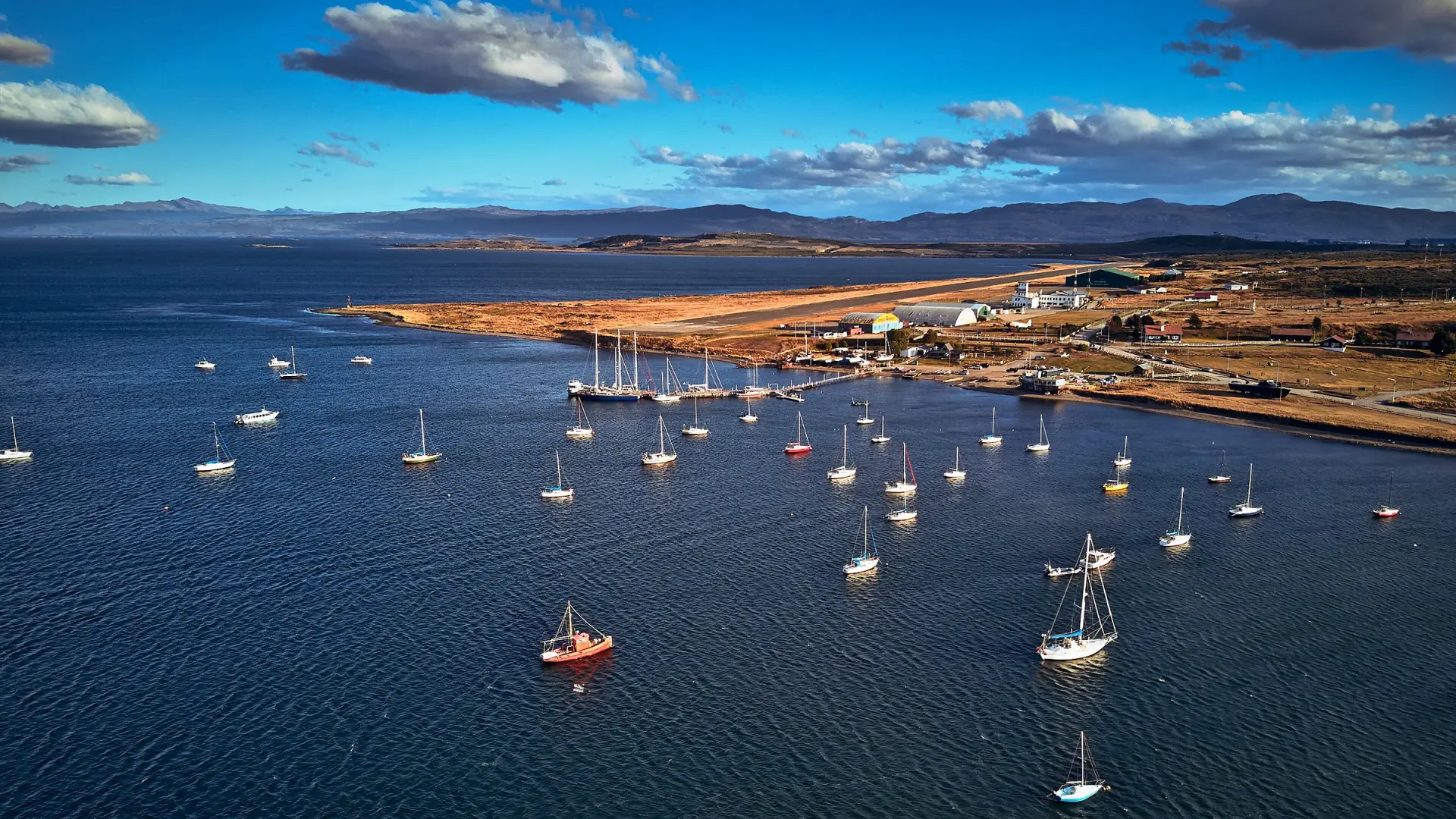Veleros fondeados en la bahía de Ushuaia vistos desde el aire, con el Canal Beagle y montañas bajas al fondo