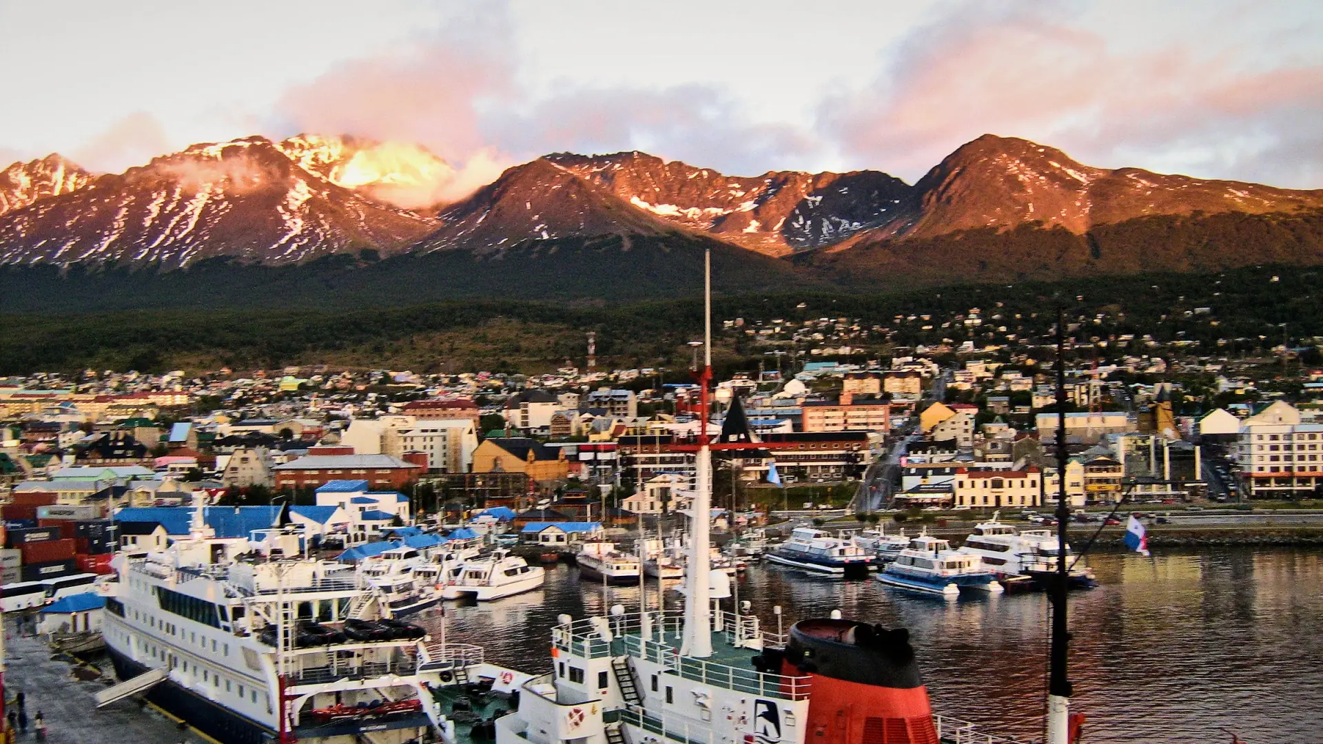 El muelle del puerto de Ushuaia con barcos amarrados, la ciudad y las montañas con luz rosada