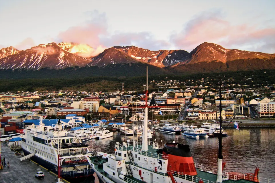 El muelle del puerto de Ushuaia con barcos amarrados, la ciudad y las montañas con luz rosada