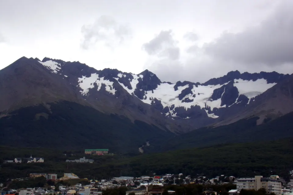 El circo del Glaciar Martial con nieve entre cumbres oscuras, sobre el bosque y las casas de Ushuaia en un día nublado