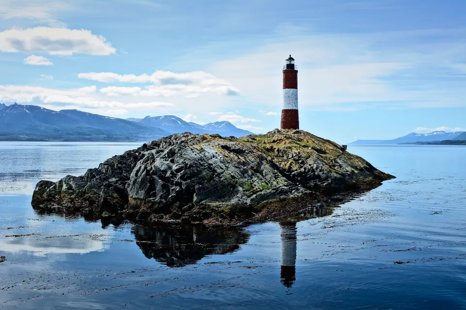 El Faro Les Eclaireurs, rojo y blanco, sobre su islote de roca en el Canal Beagle, reflejado en el agua en calma