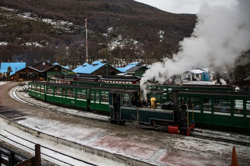 El tren a vapor en la estación, con vagones verdes, nieve y cerros en invierno