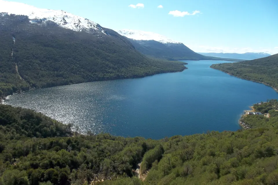 El Lago Escondido visto desde lo alto, rodeado de bosque, con cumbres nevadas a la izquierda y cielo despejado